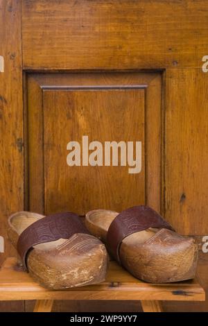 Paire de vieux sabots avec sangle en cuir sur tabouret en bois devant la porte d'entrée arrière sur l'ancienne cabane en rondins reconstruite. Banque D'Images