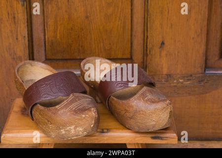 Paire de vieux sabots avec sangle en cuir sur tabouret en bois devant la porte d'entrée arrière sur l'ancienne cabane en rondins reconstruite. Banque D'Images