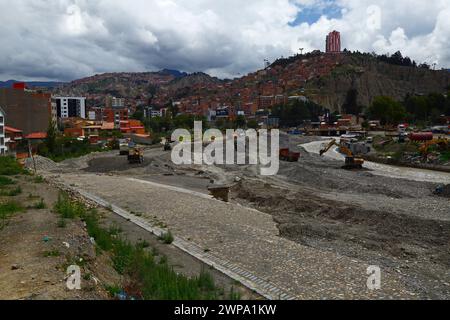 La Paz, BOLIVIE ; 6 mars 2024 : les équipes de maintenance travaillant pour les autorités de la ville de la Paz nettoient les débris et les canaux des inondations dans la rivière la Paz dans la partie inférieure de la Zona sur de la ville. Février est la saison des pluies et cette année a été l'un des mois les plus humides jamais enregistrés. De fortes pluies ont provoqué des crues soudaines, des glissements de terrain et de l'érosion dans de nombreuses vallées fluviales et des collines abruptes et instables qui font maintenant partie des banlieues de la ville. Au premier plan de cette image, des sections d'une route de liaison inachevée entre les districts de Seguencoma et de Mallasa ont été emportées. Banque D'Images