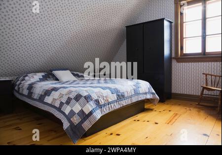 Lit double avec couvre-lit patchwork bleu et blanc sur base en bois noir dans une chambre peu meublée à l'étage à l'intérieur de la vieille maison reproduite. Banque D'Images