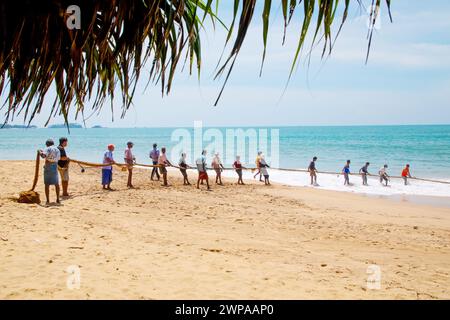 Unawatuna, Sri Lanka 09 février 2023 groupe d'hommes en vêtements d'été de différentes couleurs aidant les pêcheurs à tirer sur un grand filet de pêche de l'océan A. Banque D'Images