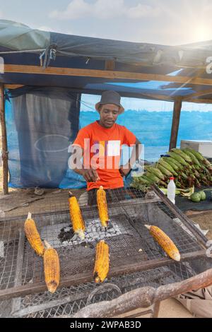 vendeur de rue africain griller du maïs doux sur le bord de la route dans une cabane Banque D'Images