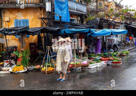 Hoi an, Vietnam ; scène de rue de la vieille ville. Jeunes femmes portant leur marchandise sur un poteau en bambou d'épaule Banque D'Images