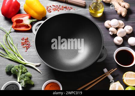 Wok en fer vide et baguettes entourées d'ingrédients sur une table en bois gris foncé Banque D'Images