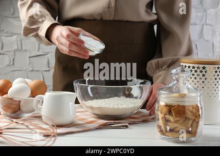 Femme ajoutant de la levure chimique dans un bol à la table en bois blanc, gros plan Banque D'Images