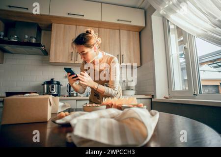 le blogueur culinaire tire des muffins au chocolat au téléphone, prépare du contenu pour les réseaux sociaux sous forme de photos et de vidéos Banque D'Images