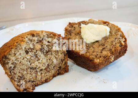 Muffin à la banane cuit maison coupé en deux avec du beurre sur une assiette blanche. ÉTATS-UNIS. Banque D'Images