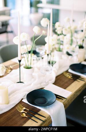 Les assiettes noires se tiennent sur des serviettes blanches à côté de bouquets de fleurs et de bougies sur la table de fête Banque D'Images