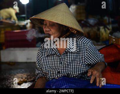 Une vietnamienne fumant un chéroot au marché aux poissons Thanh Hà à Hoi an, au Vietnam. Banque D'Images