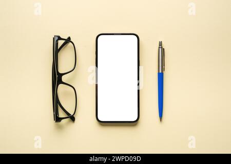 Vue de dessus des lunettes, stylo à bille et smartphone avec écran blanc sur fond jaune Banque D'Images