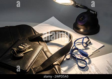 Gros plan d'un sac d'affaires mallette en cuir noir avec un assortiment d'éléments de travail, y compris des clés, des documents, un badge. Éclairé par une lampe de table Banque D'Images