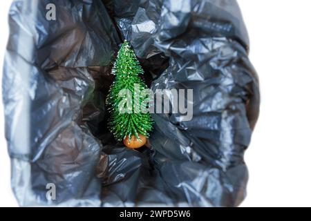 Minuscule figurine d'arbre de Noël placée à l'intérieur d'une poubelle avec un sac en plastique noir. Concept de recyclage de l'arbre du nouvel an. Banque D'Images
