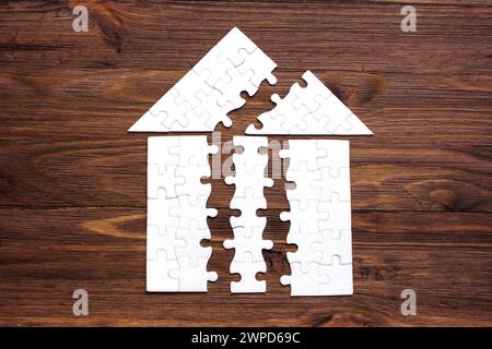 Puzzle désintégré en forme de maison couverte isolée sur un fond de bois sombre. Concept de construction et de développement. Banque D'Images