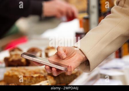 Une femme tendue la main tenant un téléphone portable, sur le point de prendre une photo ou d'effectuer un paiement en ligne à un terminal, gros plan et angle de vue bas à Pra Banque D'Images