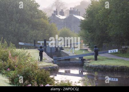 UK, Marsden, écluse du canal et maisons en pierre sur le canal étroit Huddersfield dans la brume tôt le matin. Banque D'Images