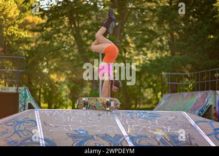 Une jeune femme faisant un stand au skate Park sur une rampe à côté d'une planche à roulettes Tempish Banque D'Images