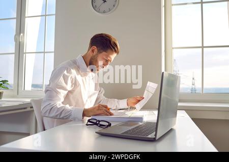 Portrait d'homme d'affaires sérieux, concentré, attrayant en chemise blanche assis au bureau écrit dans son bureau. Banque D'Images
