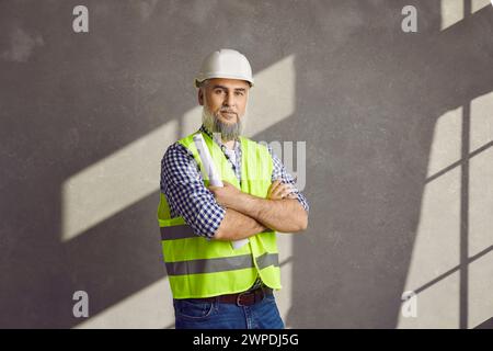 Portrait de jeune homme positif constructeur dans le casque de protection debout avec les mains pliées Banque D'Images