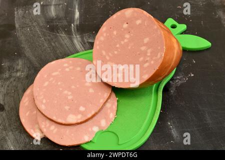 Saucisse bouillie avec des morceaux de graisse, coupée en tranches, repose sur une planche à découper. Banque D'Images