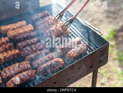 Petits méatrolls hachés roumains appelés mici ou mititei, semblables au cevapi serbe, saucisses fraîches sans peau des balkans, cuites dehors sur le barbecue Banque D'Images