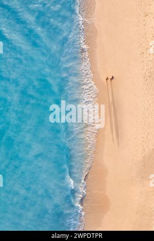 Vue aérienne romantique de couple marchant sur le coucher de soleil lumière plage longues ombres idyllique été vacances aventure humeur. Activités de loisirs en extérieur top drone Banque D'Images