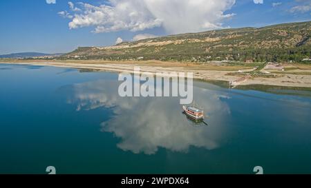 Nuages réfléchis sur le lac et un bateau voyageant sur le lac. Forêt et montagne en arrière-plan. Lac Burdur, Turquie. Banque D'Images