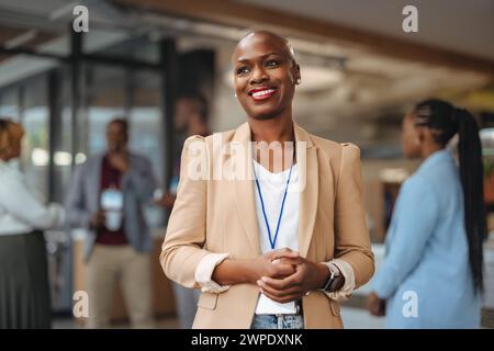 Femme d'affaires professionnelle avec un sourire radieux se tient en confiance dans un cadre de bureau moderne, reflétant la positivité et le leadership, comme ses collègues Banque D'Images