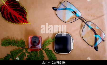 Vue de dessus de montre intelligente élégante, vernis à ongles et verre de soleil. Dans le tableau fond marron. Réflexion de la lumière Banque D'Images