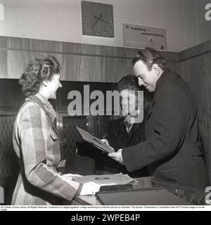 Couple en 1948. Ils sont debout dans un magasin de disques regardant la couverture d'un disque de gramophone. Une employée a plus de disques devant elle sur le comptoir. Les étiquettes sur les disques sont sa voix maîtresse. Un panneau en arrière-plan indique que « nous recevons les clients par ordre numérique ». Une façon qui n'était pas si courante à l'époque. Kristoffersson ref AM77-4 Banque D'Images