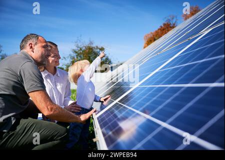 Père enthousiaste montrant le potentiel de l'énergie alternative. Famille contemporaine à la recherche de nouveaux panneaux solaires qu'ils ont achetés. Vue latérale de parents heureux et enfant intéressé à côté de panneaux solaires. Banque D'Images