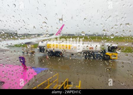 Les jours de pluie, des gouttes de pluie sur une fenêtre d'avion de ligne, diffusant le réservoir de carburant d'aviation et l'aile de l'avion, sur l'aire de trafic de l'aéroport de Londres Luton. Banque D'Images