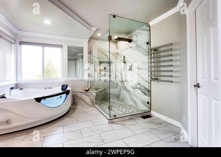 Spacieuse salle de bains principale moderne et contemporaine avec jacuzzi tube chaud et une grande douche vitrée de plain-pied plus sèche-serviettes pendant la journée lumineuse Banque D'Images