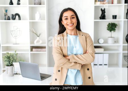 Portrait féminin.Cute confiant jeune femme d'affaires indienne ou arabe réussie, pdg, HR manager, habillé en costume élégant debout dans un espace de bureau moderne avec les bras croisés, amical souriant à la caméra Banque D'Images