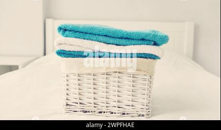 Panier à linge en osier avec des serviettes pliées propres sur le lit Banque D'Images
