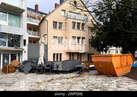 Les tables et les chaises en plastique d'un café de rue sont empilées à l'extérieur d'un bâtiment en rénovation. Conteneur orange pour déchets de construction. Banque D'Images