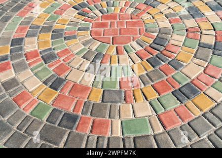 Trottoir coloré rond le jour ensoleillé dans le parc public. Pavés colorés dans la conception d'aménagement paysager de parc urbain. Cercles de tuiles dans le jardin Banque D'Images