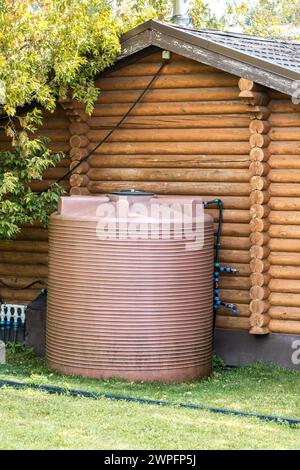 Maison en rondins soignée avec baril de trop-plein pour le remplissage de la piscine extérieure dans le jardin vert. Bâtiment rural confortable en bois naturel Banque D'Images