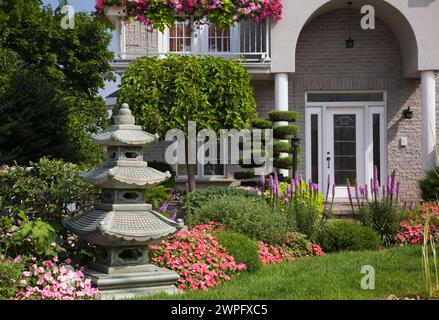 Brique grise avec garniture blanche maison de deux étages avec des Impatiens roses et rouges - fleurs de baumier et pagode en bordure dans la cour avant paysagée en été. Banque D'Images