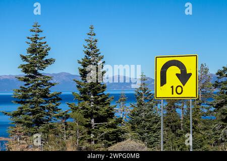 Une route de montagne surplombe un lac alpin, le lac Tahoe, avec un avertissement de circulation intense sur la conduite trop rapide de 10 km/h à l'approche d'un virage serré. Banque D'Images