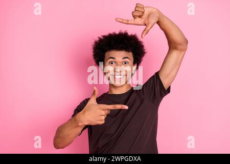 Photo de jeune photographe de gars souriant vidéaste professionnel montrant le geste de cadre pour le meilleur cadre isolé sur fond de couleur rose Banque D'Images