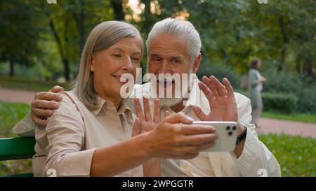 Gros plan portrait souriant caucasien couple de retraités d'âge moyen parlant relaxant à l'aide d'un smartphone en plein air parc de la ville. Heureux grands-parents en ligne Banque D'Images