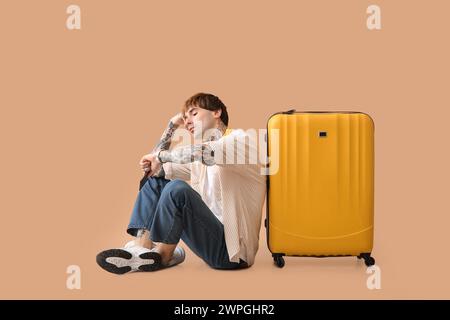 Touriste masculin fatigué avec valise regardant montre-bracelet sur fond beige Banque D'Images