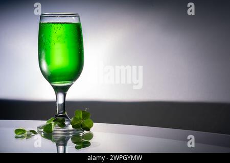 Boisson verte dans un verre clair à côté de trèfles sur une table en verre avec espace de copie à droite. Banque D'Images