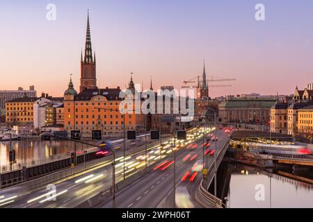Coucher de soleil sur la vieille ville de Stockholm, sentiers légers de voitures, métro et train, pont central. Ciel dégagé, bâtiments médiévaux, église Riddarholmen et île Banque D'Images