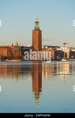 L'hôtel de ville, bâtiment de l'hôtel de ville de Stockholm, sur Kungsholmen, reflets dans le lac, au coucher du soleil, ciel bleu clair, fin d'hiver. Célèbre point de repère de SW Banque D'Images