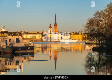 Riddarholmen église reflet dans le lac au coucher du soleil. Stockholm, Suède. Ciel bleu, bateaux au premier plan, fin hiver. Bâtiments jaunes. Banque D'Images