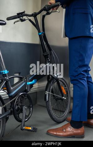 Un gros plan capture le vélo pliant électrique et les jambes d'un homme d'affaires dans un costume à l'intérieur du métro. Cette image met en évidence l'intégration des Banque D'Images