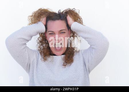 femme avec de longs cheveux bouclés et des yeux bleus regardant droit devant très en colère criant et saisissant ses cheveux Banque D'Images