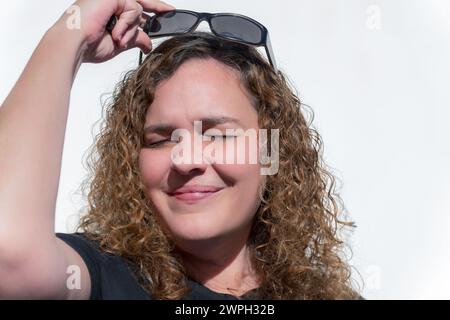 belle femme blonde aux cheveux bouclés agacée par le soleil avec ses yeux fermés met des lunettes de soleil Banque D'Images