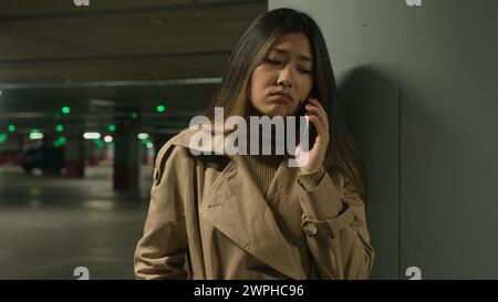 Anxieuse bouleversée femme asiatique chinoise coréenne fille japonaise femme d'affaires parler téléphone mobile à l'extérieur du parking appelant lointain déçu Banque D'Images